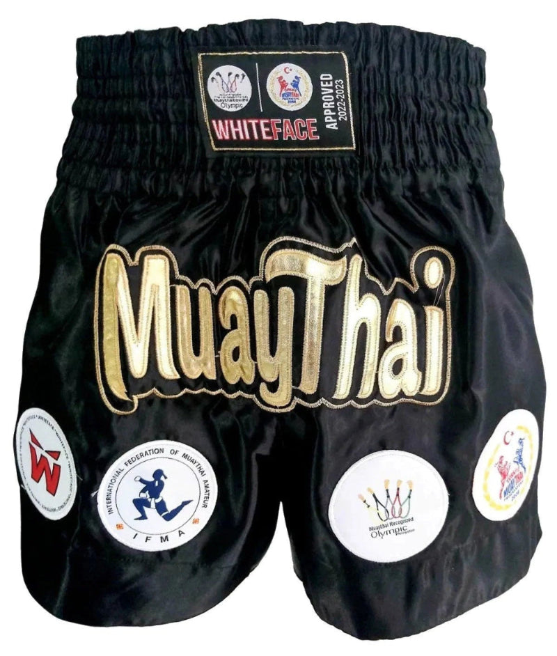 Black Muay Thai shorts with gold text and logos on a white background